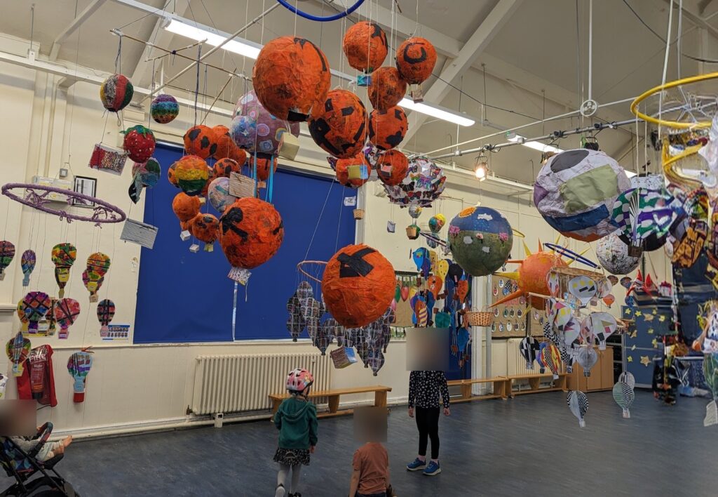 Photo of an art show at a school. A few children are visible but their faces are blurred.